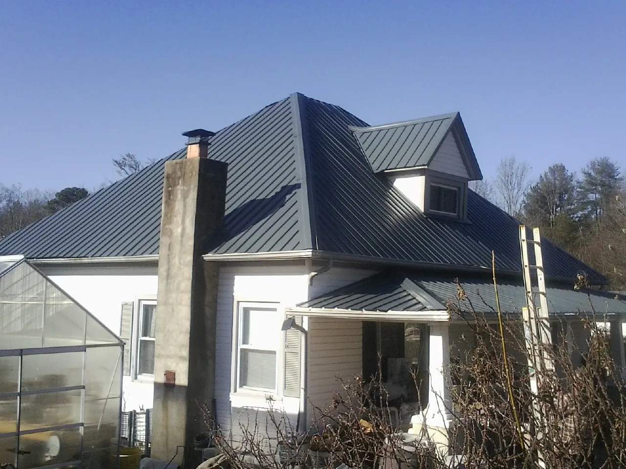 Dark blue standing seam metal roof on a white farmhouse with dormer — Slate & Tile Roof Repair by Roofing Brothers in Grandy
