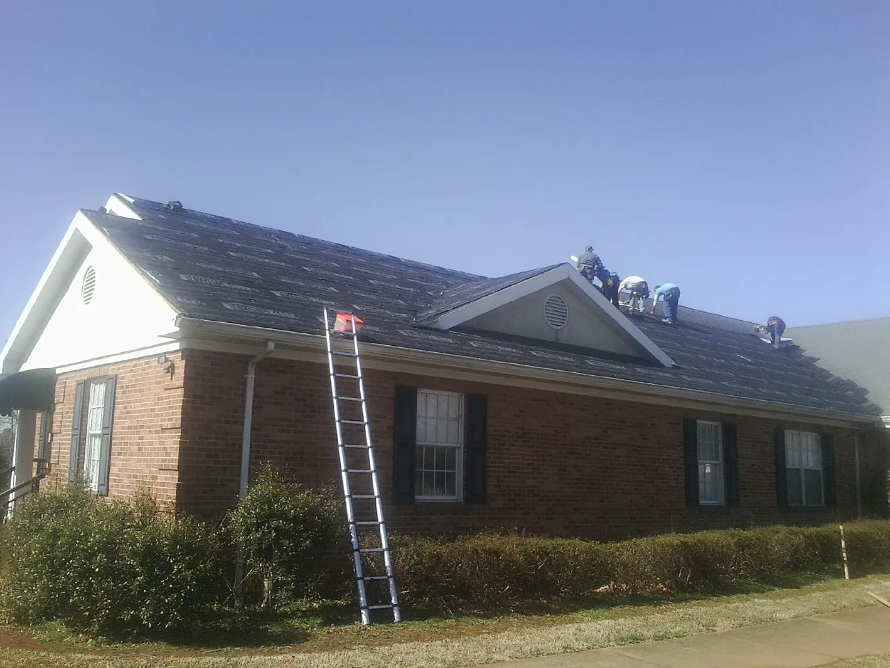 Crew tearing shingles off a brick ranch roof with a ladder set — Metal Roof Repair work by our crew in Grandy