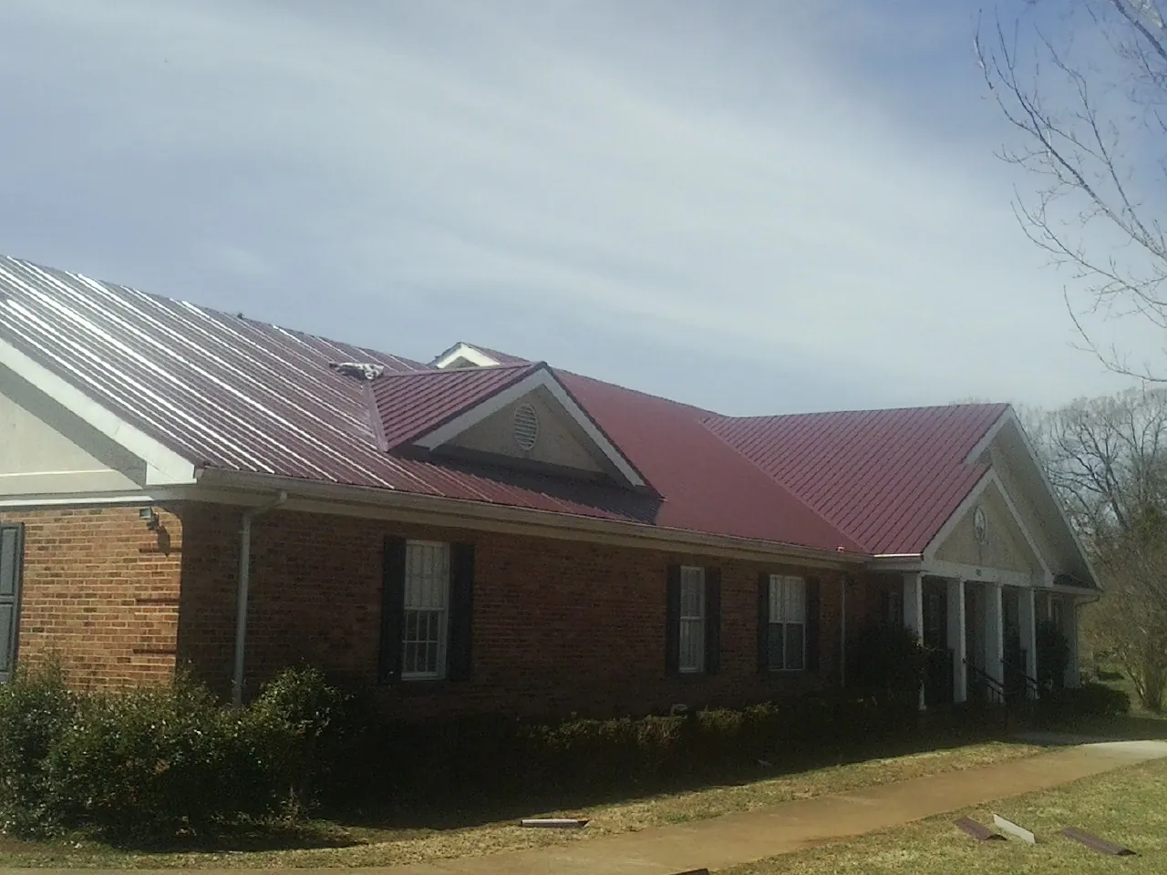 Red metal roof with gabled entries on a long brick building, from a Hail Damage Roof Repair job in Grandy