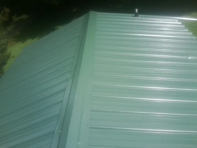 New green metal panels meeting at the ridge of a roof — Flat Roof Repair work by our crew in Grandy