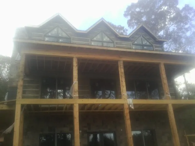 Dormers and porch framing on a large log home under construction — Roof Coating work by our crew in Grandy